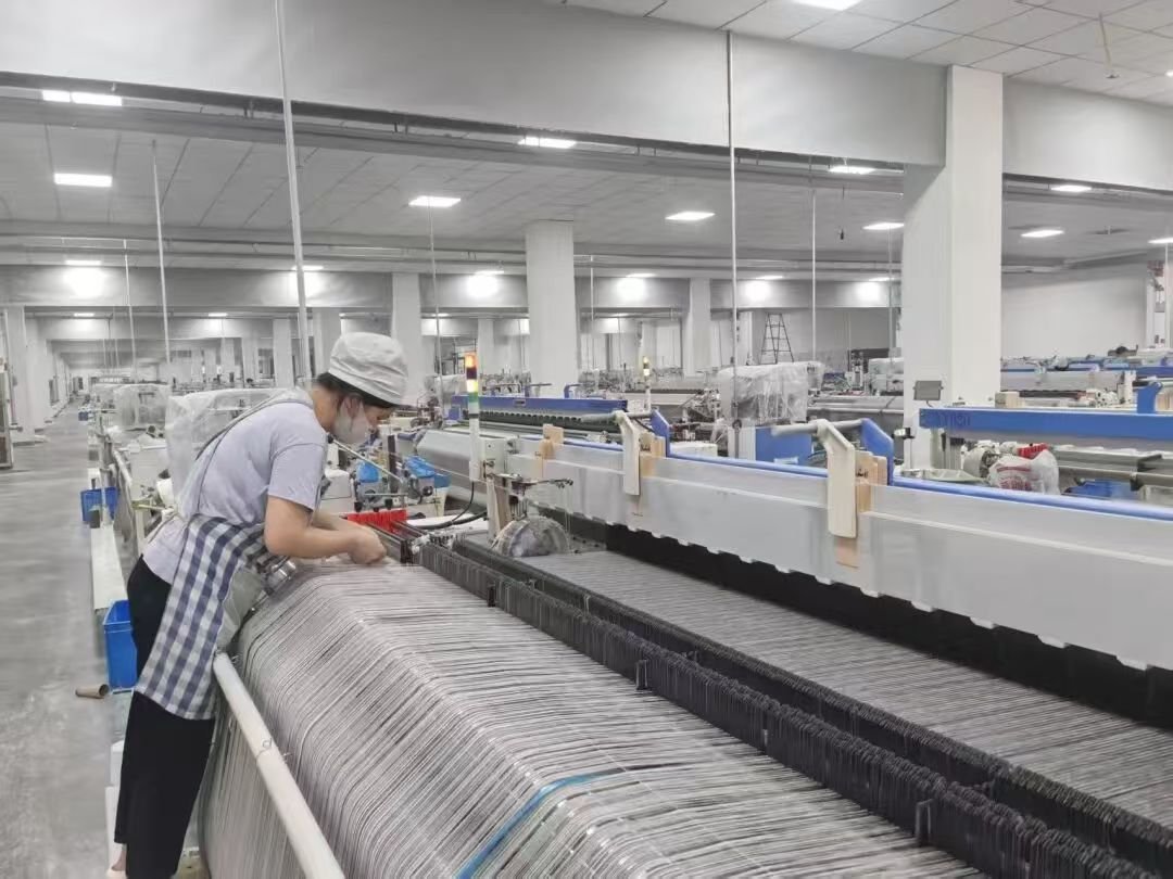 Worker standing beside a large textile machine in a production area.