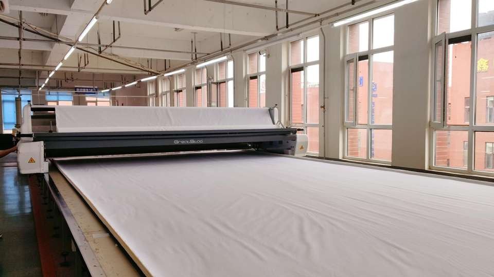 Large machine with a wide white textile sheet extending across it inside a production area.